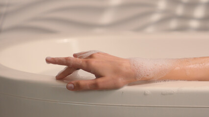 Moving shot female hand with foam woman sexy enjoying calm leisure beauty hygiene self care soapy foamy water bath tub relaxing Caucasian woman girl in bathroom listening music in headphones app spa