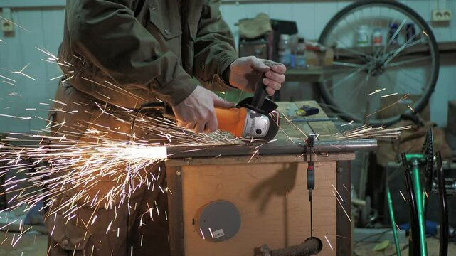 Workshop. A worker cuts a pipe fixed by clamps on a worktable with an angle grinder next to bicycles. Hand held.