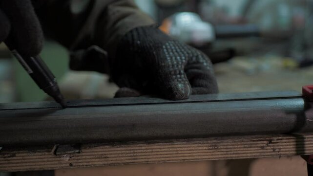 Workshop. A worker uses a steel ruler to draw a line on a pipe lying on a workbench.