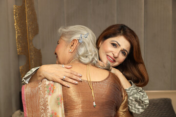 Indian happy senior mother hug to her mature daughter in living room wearing traditional dress at...