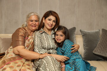 Indian happy grand mother grand daughter and mother sitting in sofa couch. wearing Indian...