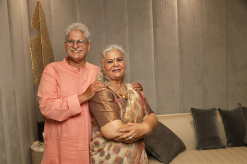 Indian happy senior couple wearing traditional dress while sitting together at sofa