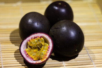 Fresh Passion Fruits with Halved Piece Displaying Juicy Seeded Pulp on Bamboo Surface