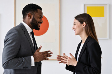 Diverse business colleagues, an african american man and a caucasian woman, having a positive and engaging discussion in a modern office or art gallery with colorful artwork