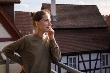 Thoughtful young woman standing on the balcony against the background of the roofs