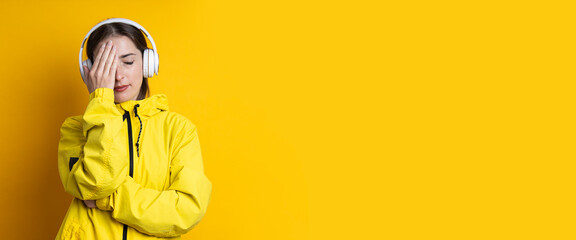 Young woman in headphones with closed eyes in a yellow jacket on a yellow background. Banner.