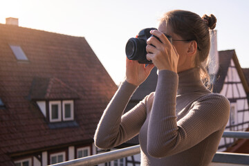 Young woman in glasses taking pictures with a camera on the terrace