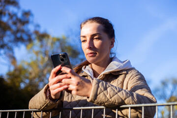 Young woman looking at the phone on the background of the autumn park