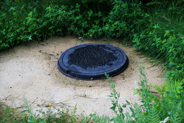 Manhole cover surrounded by grass and dirt in a natural setting on a cloudy day