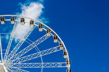 Bright Ferris wheel towers against a clear blue sky with white clouds during a sunny day