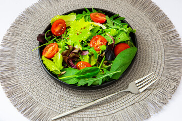 Fresh green salad with tomatoes on a textured placemat at a bright kitchen table