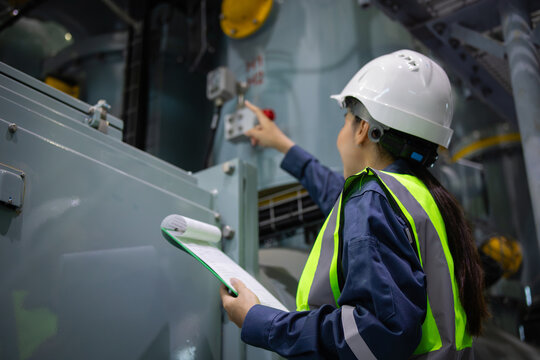 Gas insulated switchgear substation engineer inspects equipment with clipboard in industrial facility wearing safety helmet and reflective vest showing focus and professionalism
