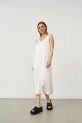 Woman in a white sleeveless dress with a V-neck, standing on a light floor wearing black platform...