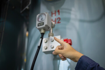 Substation engineer inspects gas insulated switchgear component carefully pointing at pressure...