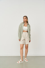 Woman in a green shirt and white top, beige shorts, and sandals stands confidently. She looks to...