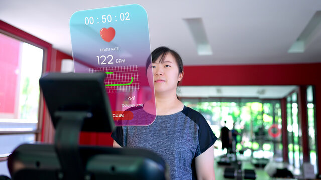 A woman running on a treadmill checks her smartwatch, which projects an augmented reality (AR) display showing real-time fitness data like heart rate, distance, and calories