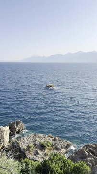 A recreational boat sails on the sea against the backdrop of a blue open sky and mountains (vertical video)