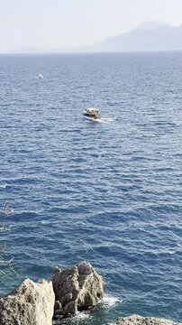 A recreational boat sails on the sea against the backdrop of a blue open sky and mountains (vertical video)