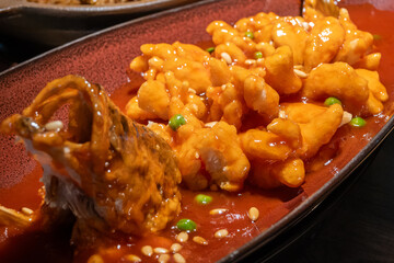A vibrant Cantonese style sweet and sour fried fish served on a red plate. Garnished with pine nuts...