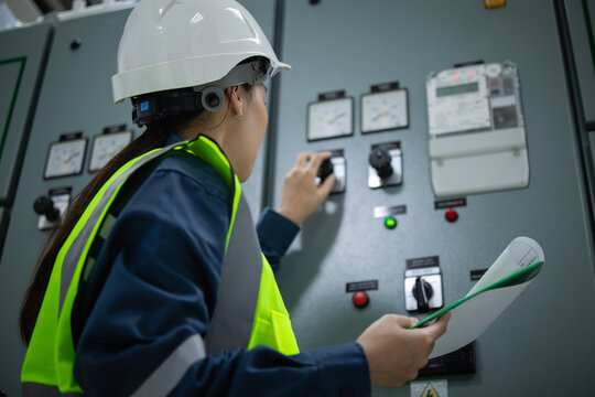 Electrical substation room engineer inspect control panel with safety helmet and reflective vest holding document for maintenance work