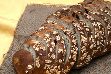 Several slices of multigrain bread rest on a wooden plate atop burlap fabric, surrounded by natural...