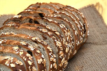 Close-up of freshly sliced oat bread with visible texture and oats on the crust, placed on burlap...