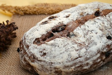 A whole loaf of artisan-style raisin bread, coated with flour, sits on a piece of burlap with...
