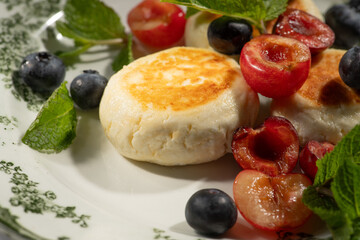 Cheesecakes arranged on a white plate, garnished with cherries, blueberries, and fresh mint, creating a delightful breakfast scene