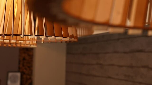 A close-up of a unique wooden slat lamp, radiating a warm, inviting glow. The camera pans along a row of these stylish decorative lights, creating ambient lighting in a modern interior, with beautiful