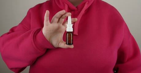 A bottle of nasal spray is held with two fingers against the background of a bright pink hoodie. A...