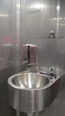 A metal sink with a soap dispenser is installed in a room with completely metal walls. The cold,...