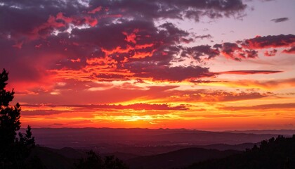 Fototapeta premium Vibrant crimson sunset stretches across cloud edges, layering warm orange and deep rose over a quiet landscape