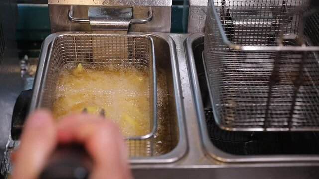 Chef deep frying  fries. Hot, bubbling oil quickly cooks potato sticks to golden crispness in a commercial fryer. Perfect for fast food, snacks, and cooking visuals.