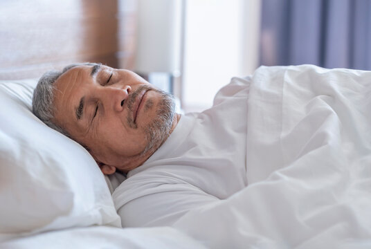 senior man laying comfortable under a white blanket,resting,bedtime sleeping in a cozy room - Powered by Adobe