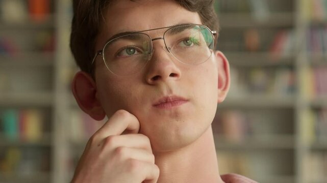 Close up hesitate Caucasian teenager guy pensive holding chin thinking decision solution difficult ponder choosing book in school college library teen boy think thoughtful education studying learning
