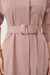 Elegant tailored mauve dress features a sleek waistband with a rectangular buckle, enhancing the...