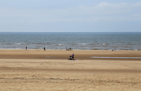 A few people enjoying the summer sunshine and large expanse of sand on Formby Beach, Lancashire, England, UK.