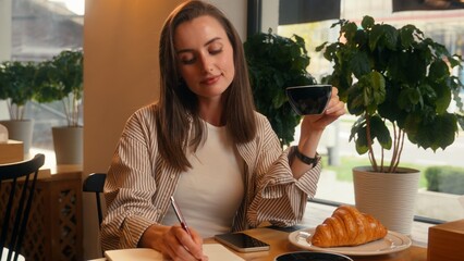 Caucasian woman in cafe inspired writing notes in notebook drinking coffee lunch happy female girl...