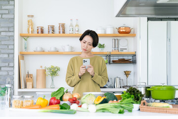 キッチンでスマホを使うミドルの主婦