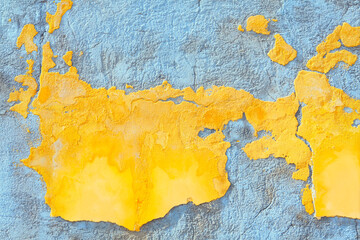 Peeling yellow paint reveals underlying gray concrete beneath. Aged concrete wall displays...
