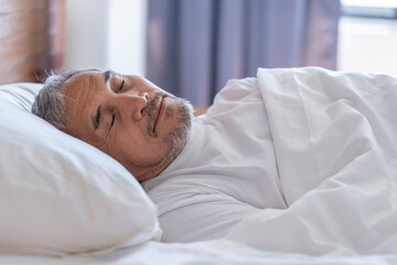 senior man laying comfortable under a white blanket,resting,bedtime sleeping in a cozy room