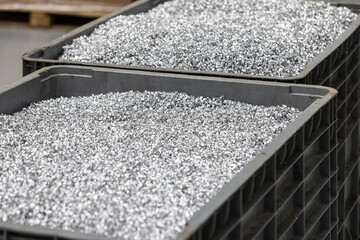 Two grey industrial bins are filled to the brim with shiny, fine metal shavings, indicative of a manufacturing process within a factory