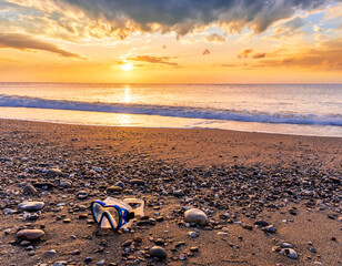 ocean cloudy morning landscape with diving mask on sea coast on foreground, sand of a beach, blue sea with surf and waves and cloudy sunset or sunrise on background