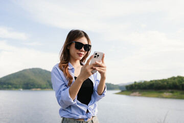 A young Asian woman leans on a white car, gazing thoughtfully at a serene mountain lake, embracing peace, nature, freedom, and the spirit of exploration.