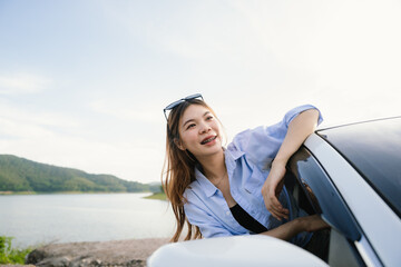 A young Asian woman smiles confidently while driving a modern car, wearing sunglasses and a seatbelt, enjoying a safe, relaxed journey filled with freedom, comfort, and joy.