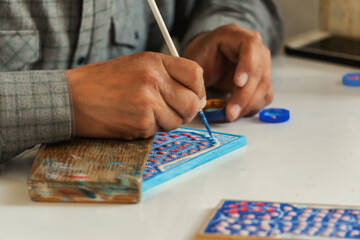 Uzbek artist hand-painting traditional ceramic tile with floral design in Samarkand, Uzbekistan