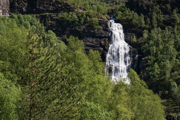 A powerful waterfall in Norway, cascading down rocks, surrounded by lush green vegetation and...