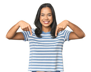 Young Latina posing in studio points down with fingers, positive feeling.