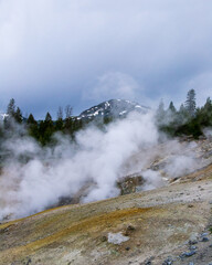 Geyser Steam over Chemically Colored Rocks and Snowy Mountains in Yellowstone

