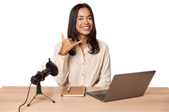 Woman records podcast with laptop showing a mobile phone call gesture with fingers. - Powered by Adobe